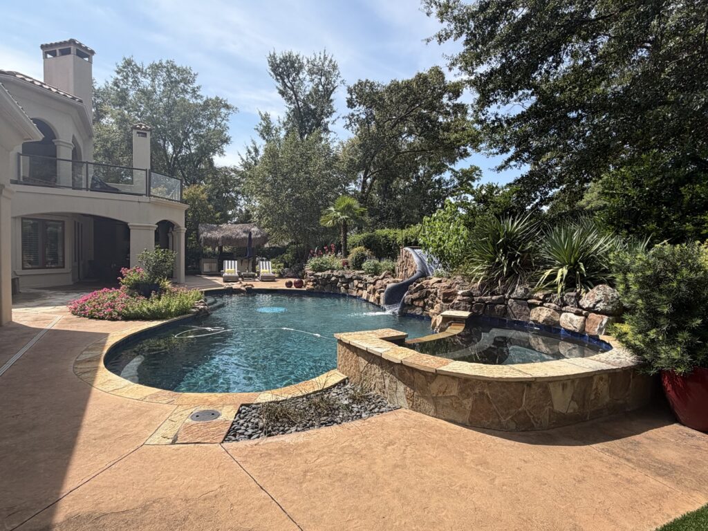 Backyard swimming pool with a raised stone spa, rock slide and landscaped garden.